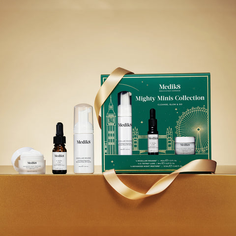 The Medik8 Mighty Minis Collection, a skincare gift set in a green box, highlights the age-defying nighttime duo of Crystal Retinal 6 and Advanced Night Restore, complemented by cream, serum, and foam products against a gold background.